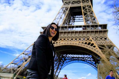 Low angle portrait of smiling woman standing against eiffel tower