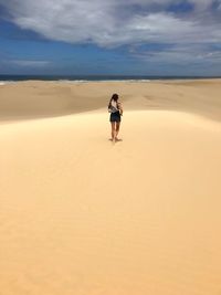 Rear view of woman running on sand dune at beach against cloudy sky