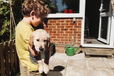 Boy holding golden retriever labrador puppy in yard