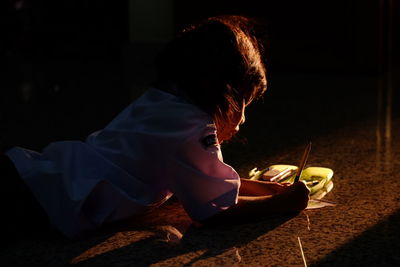 High angle view of girl writing while lying on tiled floor at home