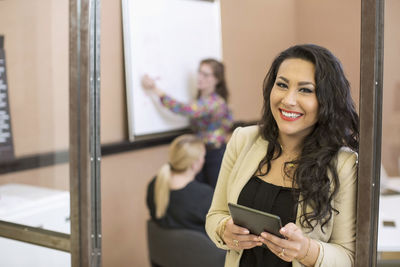 Portrait of happy businesswoman with digital tablet standing at board room entrance in office