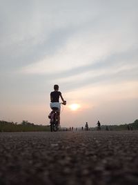 People riding bicycle on road against sky during sunset