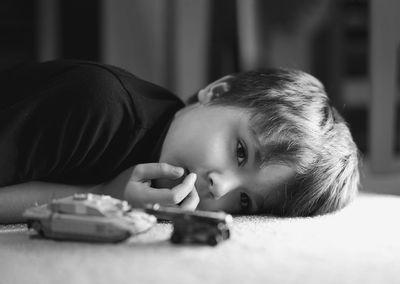 Portrait of upset boy lying on floor with toy