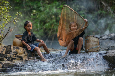 Sisters fishing while sitting at stream in forest