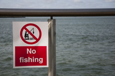 Close-up of sign board on railing against sea