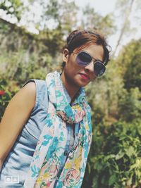 Young woman wearing sunglasses standing against trees
