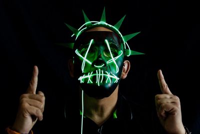 Portrait of man wearing illuminated mask against black background