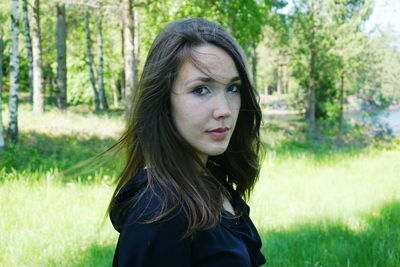 Portrait of young woman standing against trees on grassy field in forest