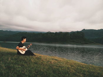 Man playing guitar on lake against sky