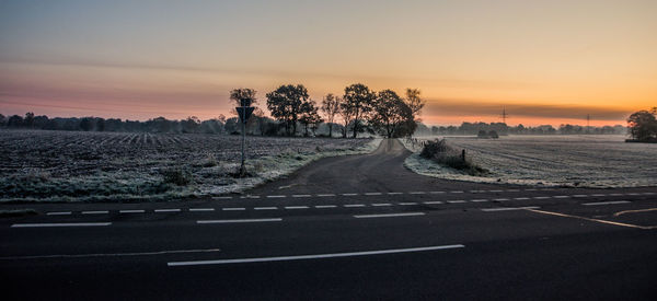 Road by trees against sky during sunset