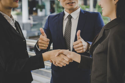 Midsection of businesswoman shaking hand while man gesturing thumbs up against railing