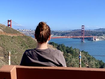 Rear view of woman looking at suspension bridge against sky