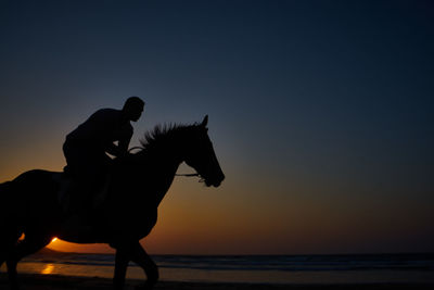 Side view of man with arms raised standing at beach against sky during sunset
