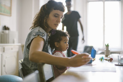 Woman working while sitting with daughter at table in house