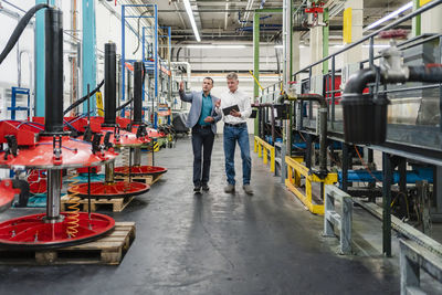 Male colleagues with digital tablet discussing on manufacturing while walking in factory