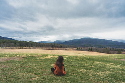 Rear view of woman sitting on grassy field against sky