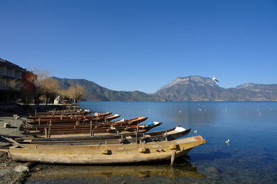 Fishing boats moored in lake against clear blue sky