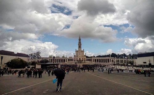 Tourists in front of building against cloudy sky