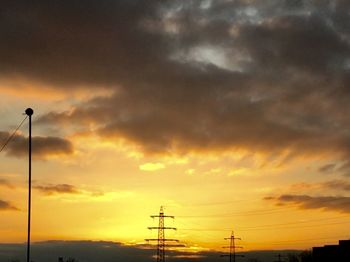 Low angle view of silhouette electricity pylon against dramatic sky