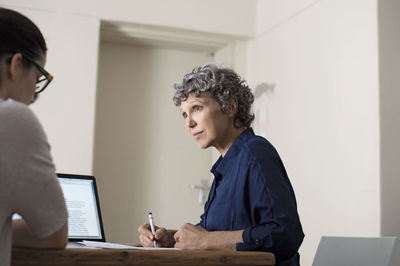 Mature woman writing while working with colleague at home