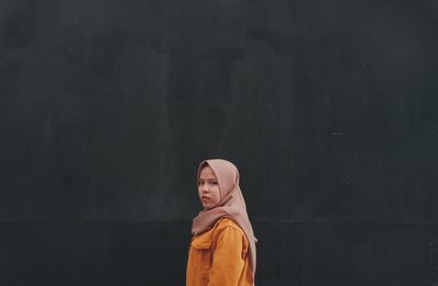 Portrait of woman standing against black background