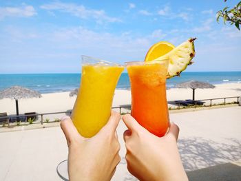 Cropped hands holding drinks against sea