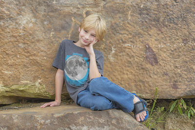 Full length of smiling boy sitting on rock