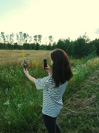 Teenage girl photographing flowers while standing on field