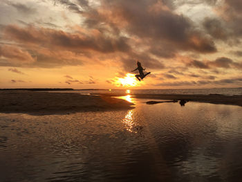 Silhouette of woman jumping on beach at sunset