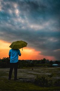 Rear view of man standing on field during sunset