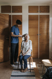 Male healthcare worker combing hair of senior woman sitting on chair at home
