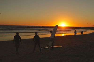 Friends enjoying at beach against clear sky during sunset