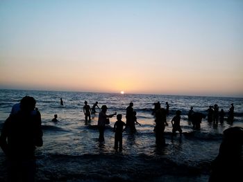 People enjoying in sea against sky during sunset