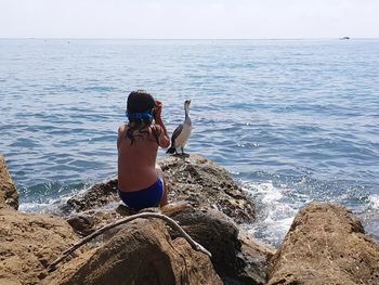 Rear view of woman on rock at sea shore against sky