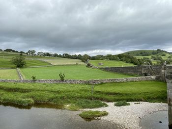 The river wharfe, passing near to the village of burnsall, with fields, trees, and cloudy weather