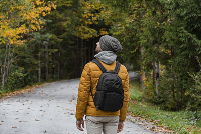 Rear view of man with backpack, walking on road through autumn woods