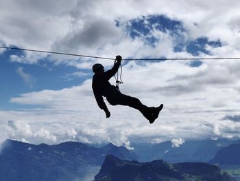 Silhouette man zip lining over mountains against cloudy sky