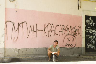 Full length of man crouching against graffiti wall