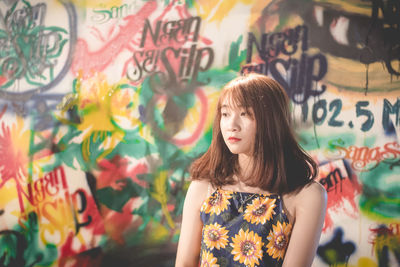 Young woman looking away while standing against graffiti wall