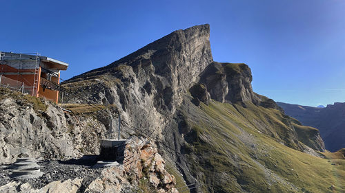 Low angle view of rocky mountain against clear blue sky