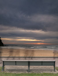 Bench by sea against sky during sunset