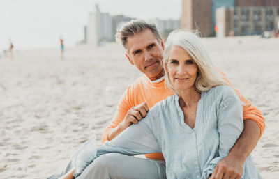 Portrait of smiling couple sitting at sandy beach
