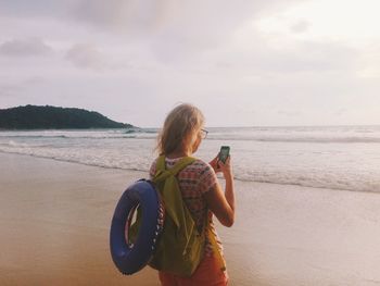 Woman using mobile phone while standing against sea at beach