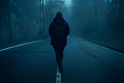 Rear view of man walking on road in forest