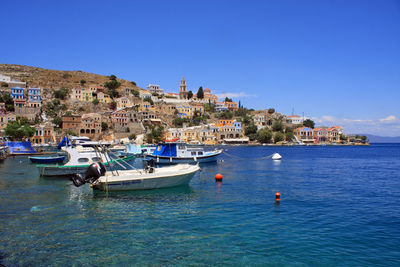 Sailboats moored on sea by buildings against clear blue sky