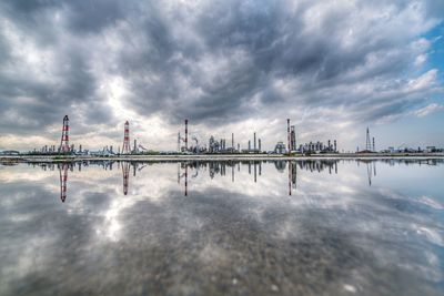 Reflection of oil refinery in water against sky