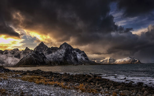 Scenic view of sea by mountains against sky during sunset