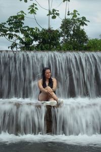 Full length of young woman sitting against waterfall
