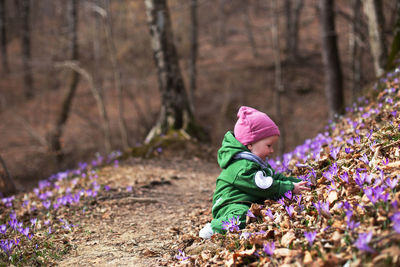 Cute toddler baby wearing green overall in forest full of wild irises. spring blossom in the forest