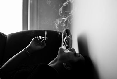 Young woman smoking cigarette while lying on sofa at home